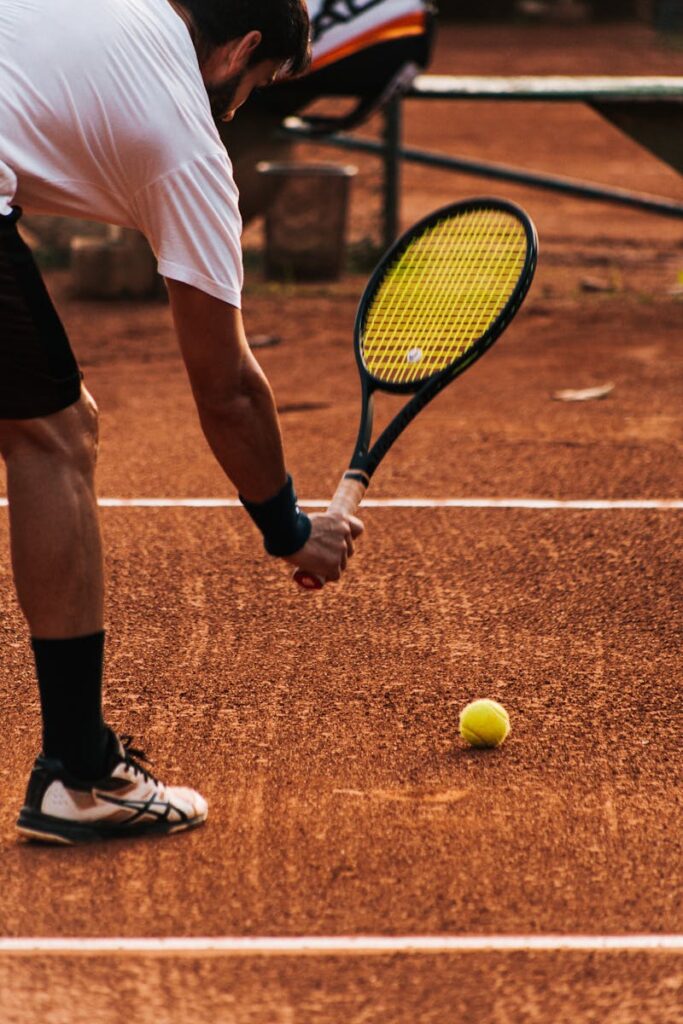 Adult tennis player on clay court getting ready to serve during a sunny day match.